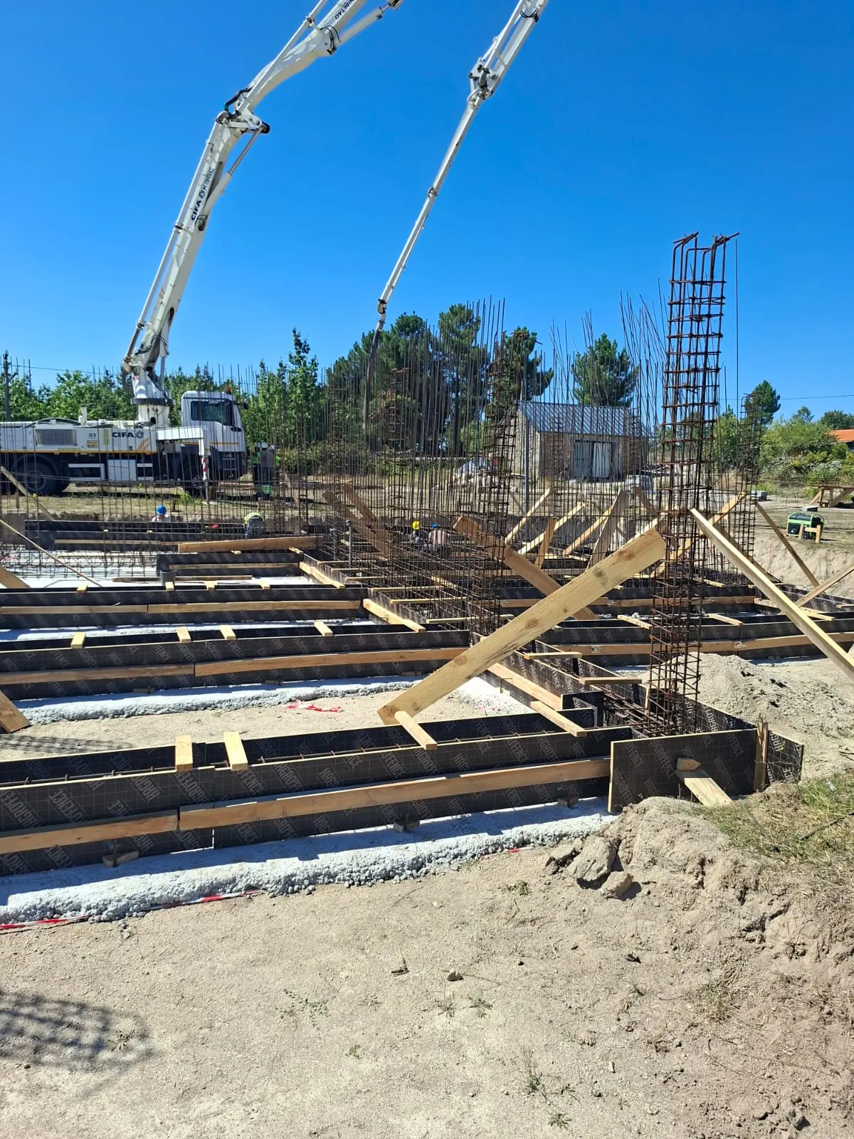 Cofragens e armaduras de fundação com equipamento de betonagem ao fundo.