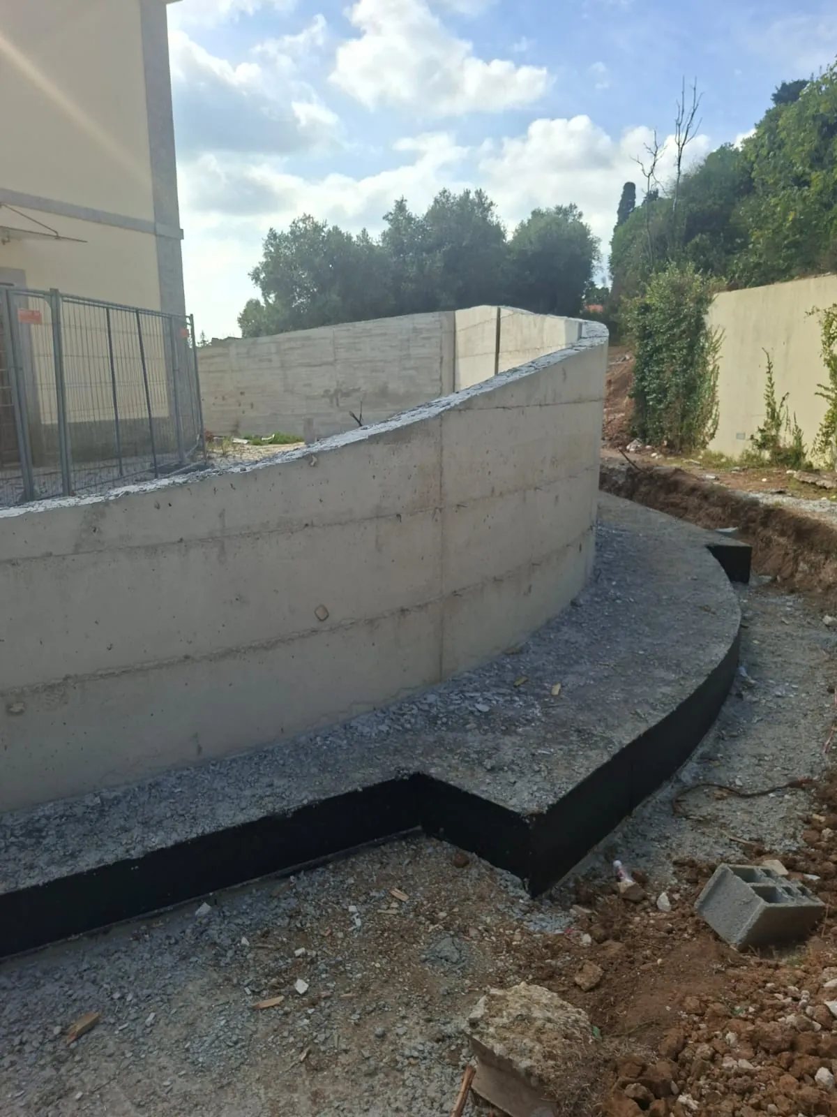 Muro curvo de betão junto a um edifício, com terreno escavado em redor.